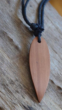Load image into Gallery viewer, The Surferkette Holz Halskette Gravur features a wooden, leaf-shaped pendant on an adjustable black cotton cord, resting on weathered wood—a natural style accessory with relaxed, effortless charm.
