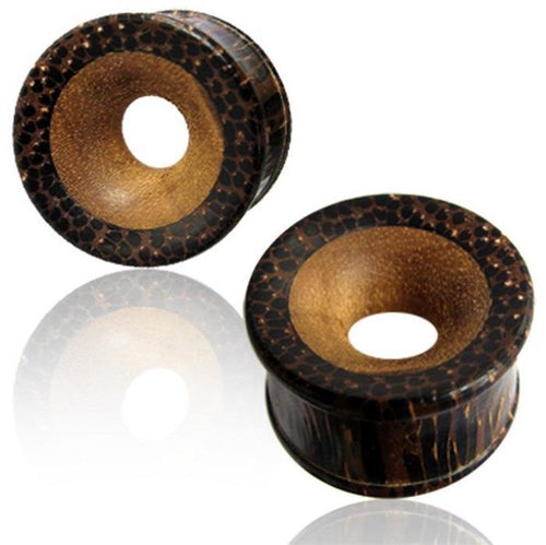 Two round, brown Palmholz Teakholz plugs with a natural tribal pattern and hand-carved smooth centers are shown on a reflective white surface. These Holztunnel feature light and dark tones for a unique, handcrafted look.