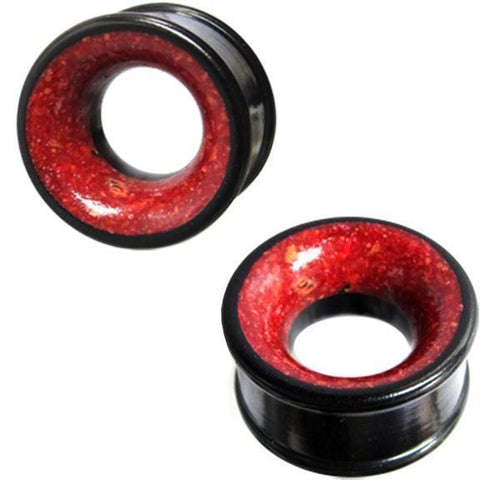 Two black Holztunnel Eisenholz gauges with red Koralleninlay are shown against a white background. The hand-carved wooden plugs feature flared edges, a hollow center, and a tribal-inspired design.