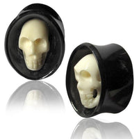 Load image into Gallery viewer, A pair of black oval Horn Plug Flesh Tunnels with white Totenkopf Bone Inlay, shown on a white reflective surface. Organic expander design for tribal piercing style.
