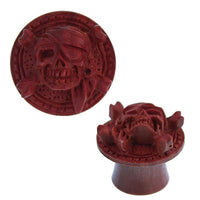 Load image into Gallery viewer, A round, rotbraun Holz Plug "Pirat Totenkopf" handgeschnitzt, double flared, features a raised skull with eye patch and headscarf over crossed bones, blending classic pirate motifs with artisanal woodwork.
