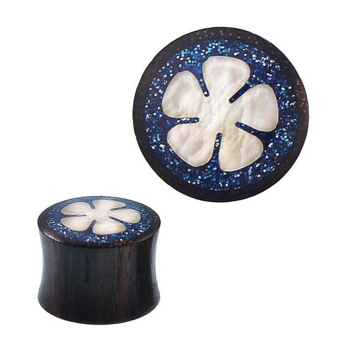 A Plug Sonoholz Resin Glitzer Inlay blau Perlmutt Blume Tunnel Tribal Expander, shown in round black design with blue glittery inlay and a white Perlmutt Blume design in the center, displayed from top and side views.