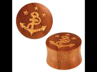 Load image into Gallery viewer, The "Holz Plug braun handgeschnitzt Lasergravur Anker Sterne gold bemalt Tunnel Expander" zeigt ein handgeschnitztes, rundes Plug: Ein Anker mit Schlange und drei goldenen Sternen ist per Lasergravur verziert; einer steht, einer liegt zur Formansicht.
