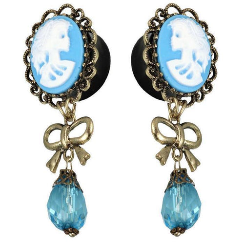 Vintage-style earrings: blue and white acrylic cameo skeleton woman, gold brass border, bow accent, faceted blue glass teardrop pendants—Plug Piercing.