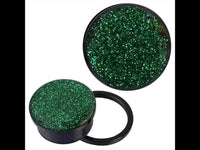 Load image into Gallery viewer, A pair of Schraub Plug Tunnel Acryl schwarz grüner Glitzer Piercing Ohrschmuck rests on a white background. One plug stands upright, displaying its green glitter top, while the other lies on its side with a black ring next to it.
