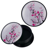 Load image into Gallery viewer, The Schraub Plug Acryl schwarz pink Blütenzweige Piercing Ohrschmuck features a round black container with a white lid decorated with pink flower branches—ideal for storing your stylish piercing jewelry.
