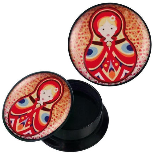 A round black container with a lid showing a vibrant Matroschka design in red, yellow, and blue, resembling the Schraub Plug Acryl rot gelb blau Matroschka Piercing Ohrschmuck. The lid appears both on and next to the open container.