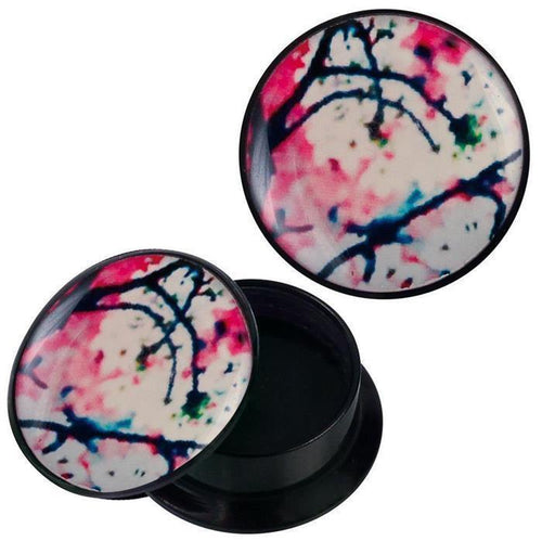 A round black Acryl Schraub Plug, "Schraub Plug Acryl Kirschblüten groß rosa weiß schwarz Piercing Ohrschmuck," with a removable lid and abstract pink, blue, and green ink-art design, is shown partially open with an empty interior.