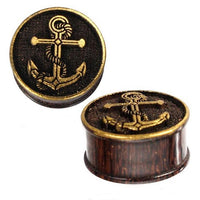 Load image into Gallery viewer, Two dark brown Plug Holz Tamarinde ear plugs feature a golden brass anchor with rope design and a raised rim. They have a wood-like texture and are perfect as unique, stylish piercings.
