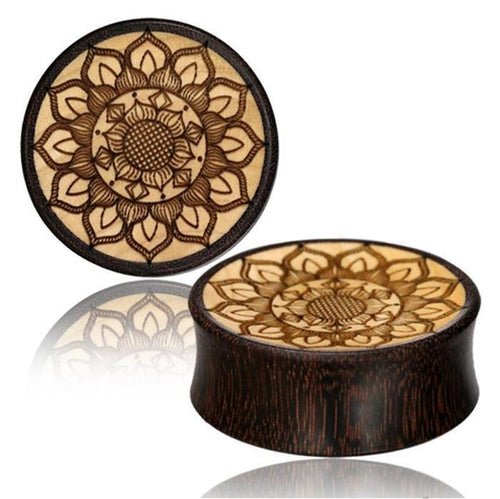 Two round Plug Holz Tamarinde Krokodilholz plugs in light and dark tones, each engraved with a detailed Mandala Blüte Gravur, are displayed on a white background with subtle reflections beneath them.