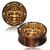 Load image into Gallery viewer, Plug Holz hell dunkel Tribal Maske Gravur double flared is a round wooden plug with a tribal mask engraving, crafted from tamarind wood. It features decorative patterns and natural light and dark brown tones for a striking finish.

