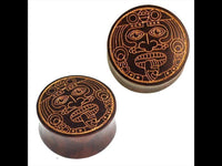 Load image into Gallery viewer, Two round, dark brown Holz Plugs by Sonoholz with golden engraved designs of a warrior mask face. Featuring detailed eyes, nose, mouth, and a tongue for an authentic look.
