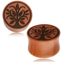 Load image into Gallery viewer, Two round, brown Holz Plug Sawoholz Tunnel Expanders, hand-carved with a Baum des Lebens design of stylized leaves and branches; one stands upright, the other lies on its side, showing both the intricate engraving and shape.
