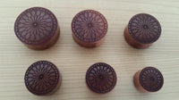 Cargar imagen en el visor de la galería, Six round brown Sawo wood plugs with black engraved floral and heart tribal patterns are displayed on a light wooden surface.

