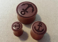 Load image into Gallery viewer, Three Flesh Plug Sawoholz Anker Seil Ring double flared Lobe Dehner plugs in red-brown, each engraved with an anchor inside a circular border, are displayed on a beige surface.
