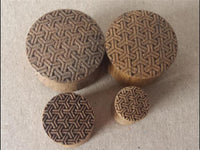 Load image into Gallery viewer, Four round Flesh Plug Teakholz Peace Knoten Muster double flared Lobe Dehner in brown, each engraved with intricate geometric patterns, are arranged on a plain surface.

