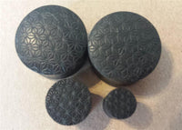 Load image into Gallery viewer, Four black Flesh Plug Ebenholz Stern Blume des Lebens double flared Lobe Dehner with engraved geometric flower-of-life design are grouped together on a light brown surface.
