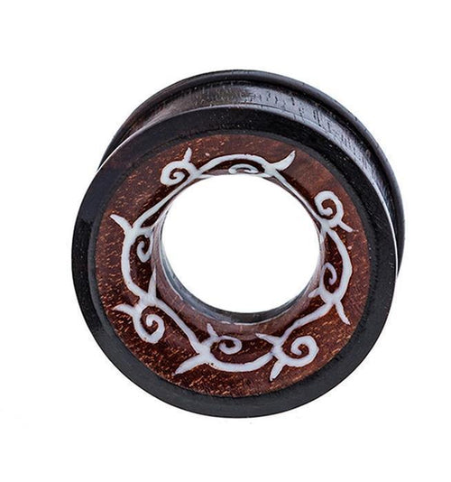 The Holz Tunnel Bone Inlay Kranz Spiralen Tribal Plug is a hand-carved, circular expander made from Sonoholz and Tamarindenholz, featuring a hollow center and intricate light-colored vine and swirl designs around the edge.