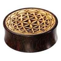 Load image into Gallery viewer, A round Plug Holz Tamarinde Krokodilholz with a “Blume des Lebens” (flower of life) geometric pattern and zigzag edge, featuring interlocking shapes in contrasting wood tones.
