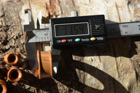 Load image into Gallery viewer, A digital caliper measures the diameter of an Olivenholz Flesh ribbed Tunnel Lobe Piercing Holz straight, showing 11.54 mm on the screen, with handgeschnitzt wooden pieces nearby on a textured wooden surface.
