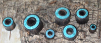 Load image into Gallery viewer, Seven Flesh Tunnel Eisenholz schwarz Rim Crushed Türkis Inlay ear plugs are displayed on rough tree bark, showcasing their turquoise inlays. The plugs range in size, each featuring striking blue-green accents.
