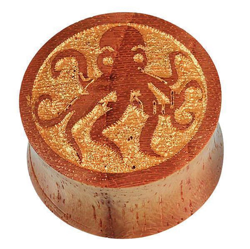 The Teakholz Plug braun gold bemalt Oktopus double flared features a round wooden design with a polished finish and a detailed octopus engraving on top, highlighting its intricate craftsmanship.