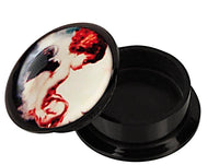 Load image into Gallery viewer, A black Schraub Plug Acryl "Engelchen sitzend" container with its lid slightly open, showing colorful abstract face art in red, white, and black—perfect for storing your Piercing Ohrschmuck.
