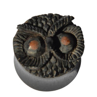 Load image into Gallery viewer, The "Holz Plug Eule schwarz handgeschnitzt braune Augen" is a small, round wooden plug with an owl’s face, brown eyes, and feather details—an elegant organic Schmuck piece shown on a plain white background.
