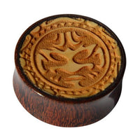 Load image into Gallery viewer, The Plug Holz hell dunkel Tribal Maske Gravur double flared is a round, double-flared wood plug with a carved stylized tribal mask design on its surface, shown from above against a white background.
