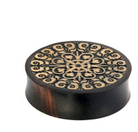 Load image into Gallery viewer, A round, dark wooden box with a flat lid displays an intricate symmetrical cross and scrollwork pattern in light wood, echoing the hand-carved style of the Holz Flesh Plug Tamarinde Holz Krokodilholz Kreuz Ranken.
