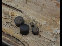 Load image into Gallery viewer, A set of four dark Holz Plug Kokosholz Inlay handgeschnitzt Sonoholz ear plugs, each with textured circular patterns and varying sizes, is displayed clustered on rough light brown wood.

