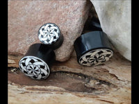 Load image into Gallery viewer, Three Plug Horn weiß Gravur schwarz Bänder Blende Sternmuster with white star patterns are displayed on textured wood between two large rocks.
