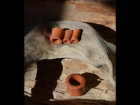 Load image into Gallery viewer, Four cylindrical objects of the Holz Tunnel rot braun fein gemasert konvex Rosenholz rest on textured wood, three grouped at the top and one larger below, all bathed in natural light.
