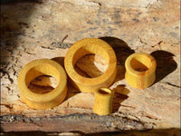Load image into Gallery viewer, Four "Jackfrucht Holz Tunnel ocker Pünktchen konvex dick" wooden rings of different sizes are arranged on a textured wooden surface, with sunlight creating shadows across the rings and the background.
