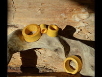 Load image into Gallery viewer, Four Jackfrucht Holz Tunnel ocker Pünktchen konvex dick rings rest on driftwood against a sunlit wooden background, with shadows and light highlighting their yellow tone and the natural wood grain.
