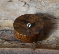 Load image into Gallery viewer, A round, dark brown Flesh Plug Holz Parasitholz braun double flared with a shiny metal knob rests on textured wood, serving as a decorative or functional handcrafted item.
