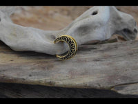 Load image into Gallery viewer, The Saddle Plug Messing antik gold Sichel Bögen Tunnel pendant, featuring crescent-shaped decorative swirls inspired by Sichel Tunnel designs, is displayed on smooth driftwood with more pale driftwood in the background.

