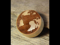 Load image into Gallery viewer, A Flesh Plug Weltkarte Holz Welt Erde Globus double flared, engraved with a map of Europe and Africa, rests elegantly on a rustic wooden surface.
