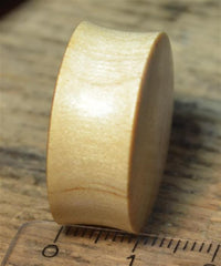 Load image into Gallery viewer, A smooth, light-colored Flesh Plug Weltkarte Holz Welt Erde Globus double flared with a slightly concave surface stands upright on wood next to a ruler for scale.

