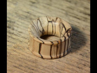 Load image into Gallery viewer, A handcrafted Bananenholz Flesh Tunnel hell ribbed straight konkav with a wide band and natural dark streaks rests on a textured wooden surface.
