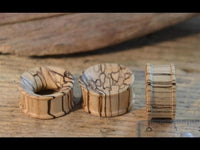Load image into Gallery viewer, Three handcrafted Bananenholz Flesh Tunnel hell ribbed straight konkav plugs, each showing dark natural grain patterns, are displayed on a wooden surface next to a ruler for scale, highlighting front, back, and side views.
