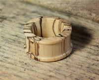 Load image into Gallery viewer, A ribbed, straight konvex Bananenholz Flesh Tunnel in a light finish with natural grain patterns rests on a rustic wooden surface.
