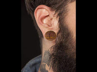 Load image into Gallery viewer, A close-up of a bearded person with a neck tattoo, wearing a Krokodil Holz Plug Baum des Lebens hell double flared engraved with a tree design. The person is dressed in a dark shirt.

