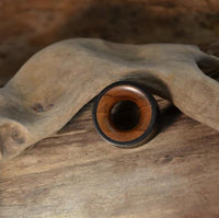 Load image into Gallery viewer, The handmade Holz Tunnel schwarz braun aus Eisenholz und Teakholz sits on curved driftwood atop a rustic wooden surface.
