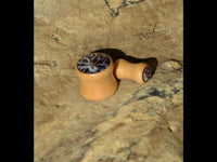 Load image into Gallery viewer, A small, tan wooden pipe with dark decorative patterns on the bowl and mouthpiece, set on a light brown stone—evoking the intricate design of the Holz Plug Oktopus Krake Bild beige hell double flared.
