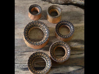 Load image into Gallery viewer, Six handmade Holz Plug Olivenholz Sonnenblume double flared rings with intricate black geometric patterns are arranged on wood. The rings, ideal as piercing or flesh tunnel jewelry, feature beveled edges and detailed outer designs in various sizes.
