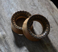 Load image into Gallery viewer, Two handmade Holz Plug Olivenholz Sonnenblume double flared ear plugs, adorned with detailed sunburst carvings, rest on textured wood—perfect for those wanting a unique and natural-style piercing accessory.
