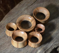 Load image into Gallery viewer, Five handmade Holz Plug Olivenholz Sonnenblume double flared pieces, featuring smooth surfaces and visible grain patterns, are arranged on a rustic wooden background, showcasing their unique natural wood texture.
