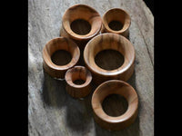 Load image into Gallery viewer, Seven handmade Holz Plug Olivenholz Sonnenblume double flared plugs of various sizes are arranged on textured wood, showcasing their smooth finish and natural grain—perfect for those seeking distinctive wooden flesh tunnel jewelry.
