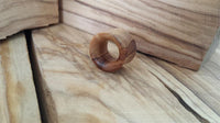Load image into Gallery viewer, A small, smooth, round Olivenholz Flesh Tunnel Ohr Piercing Holz Double Flared sits on a light wood surface with visible grain and blocks in the background.
